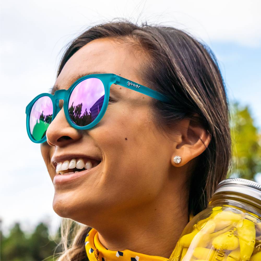 Óculos de sol verde unissex com armação redonda e lente roxa espelhada, polarizada com proteção UV400. O acessório é leve, confortável e não escorrega ou pula no rosto ao realizar esportes.