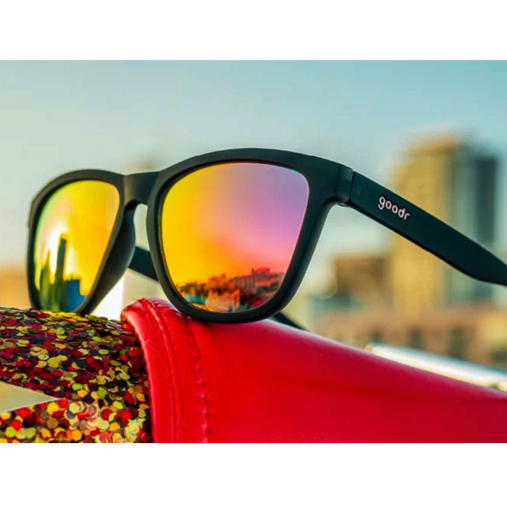 Óculos de sol preto unissex com armação quadrada e lente rosa espelhada, polarizada com proteção UV400. O acessório é leve, confortável e não escorrega ou pula no rosto ao realizar esportes.