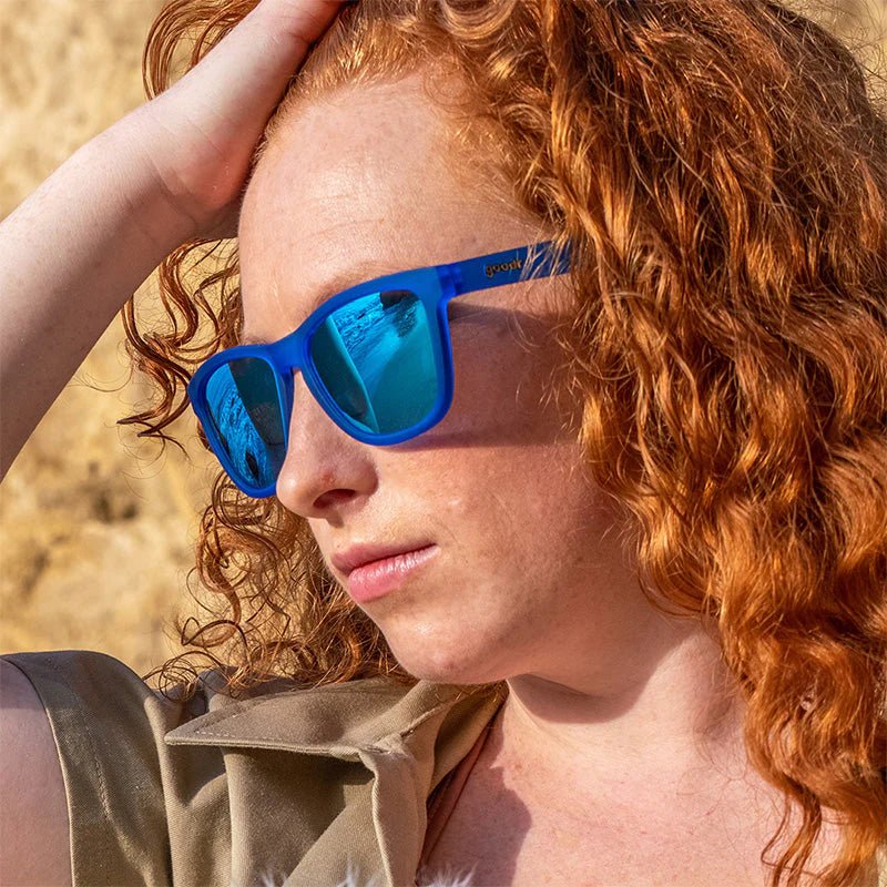 Óculos de sol azul unissex com armação quadrada e lente azul espelhada, polarizada com proteção UV400. O acessório é leve, confortável e não escorrega ou pula no rosto ao realizar esportes.