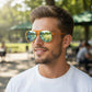 Homem usando óculos de sol Goodr Brasil modelo aviador com armação amarela e lentes espelhadas azuis em ambiente externo