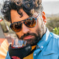 Homem usando óculos de sol Goodr Brasil modelo aviador com armação azul e lentes amarelas degradê em ambiente externo.
