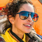Mulher usando óculos de sol Goodr Brasil modelo aviador com armação azul e lentes amarelas degradê em ambiente externo