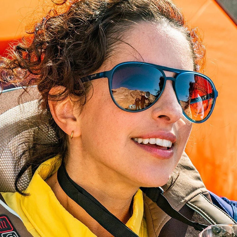 Mulher usando óculos de sol Goodr Brasil modelo aviador com armação azul e lentes amarelas degradê em ambiente externo