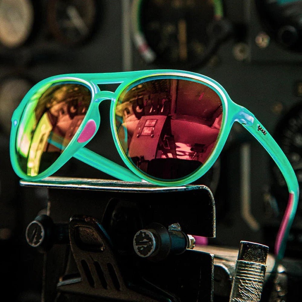 Óculos de sol Goodr Brasil modelo aviador com armação verde, detalhes em rosa e lentes espelhadas amarelas polarizadas.