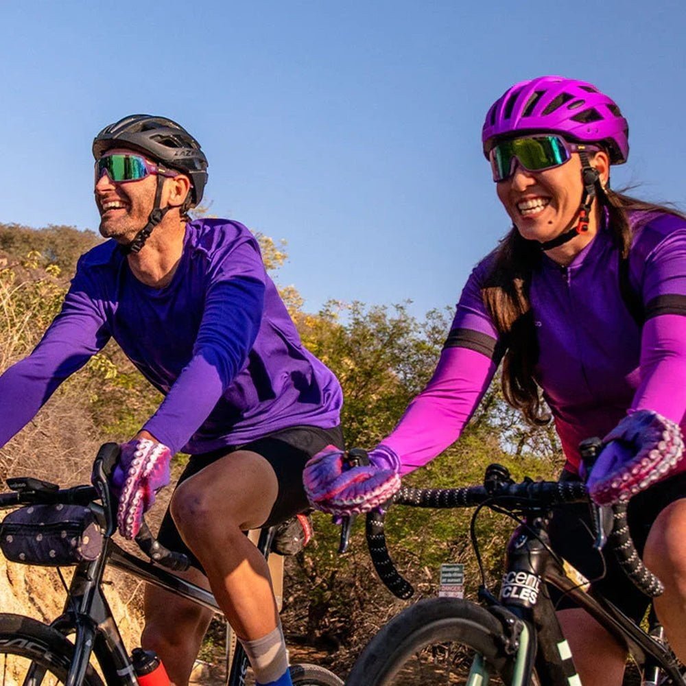 Ciclistas usando óculos Goodr Brasil roxos com lentes verdes espelhadas durante pedalada ao ar livre