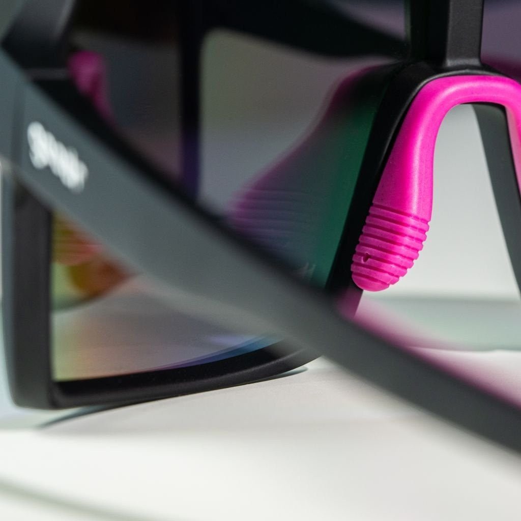 Detalhe da ponte nasal rosa e armação preta dos óculos esportivos Goodr Brasil com lentes roxas espelhadas.