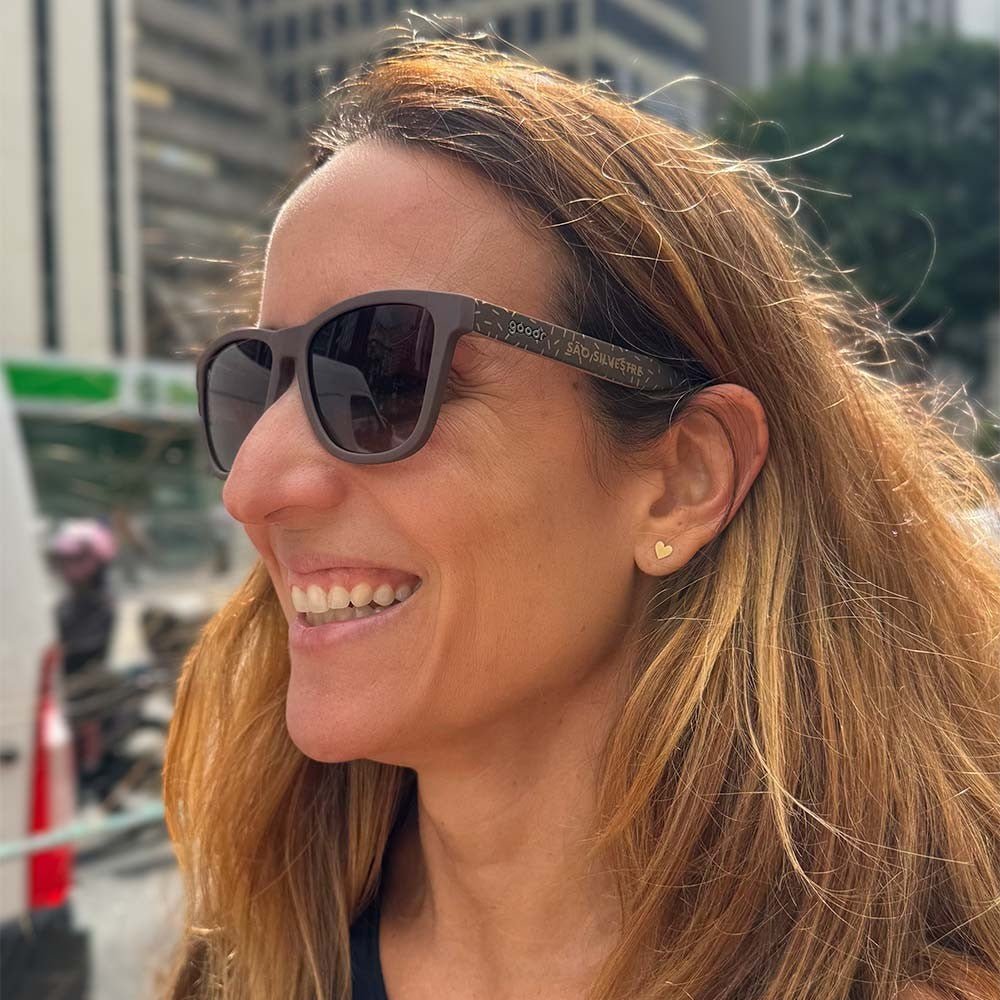 Mulher sorrindo usando óculos de sol Goodr Brasil marrom da edição limitada São Silvestre com detalhes de brigadeiro.