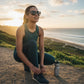 Mulher usando óculos Goodr Brasil Always the Main Event cinza polarizado em trilha ao pôr do sol, estilo esportivo.