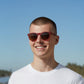 Homem usando óculos de sol Goodr Brasil modelo Circle G com armação bordô e lentes marrons polarizadas ao ar livre