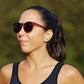 Mulher usando óculos de sol Goodr Brasil modelo Circle G bordô com lentes marrons polarizadas em ambiente externo.