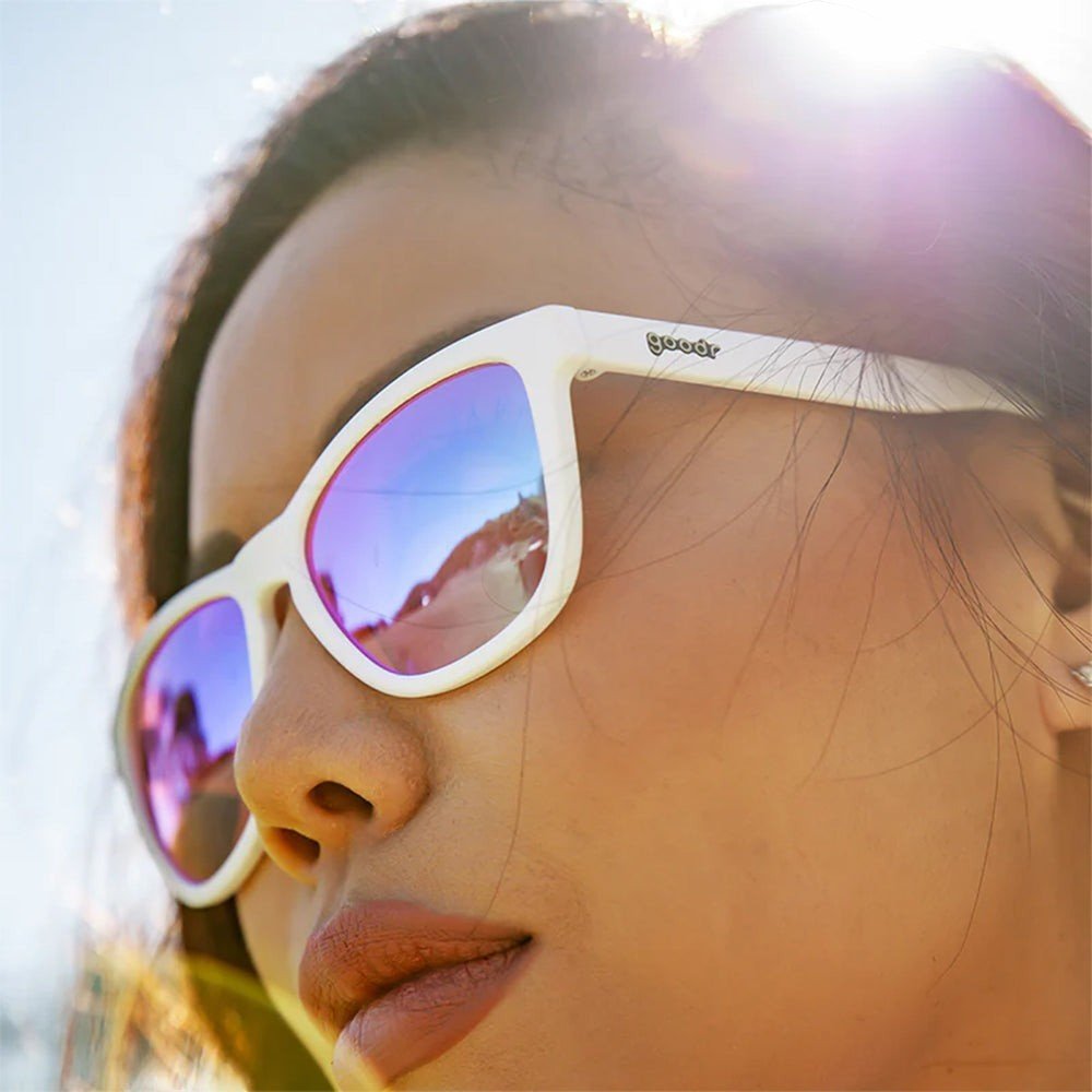 Mulher usando óculos de sol Goodr Brasil Au Revoir, Gopher com armação branca e lentes rosa polarizadas ao ar livre.