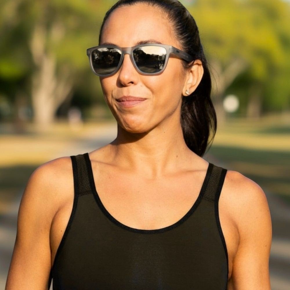 Mulher usando óculos de sol Goodr Brasil cinza com lentes espelhadas polarizadas em ambiente externo ensolarado.