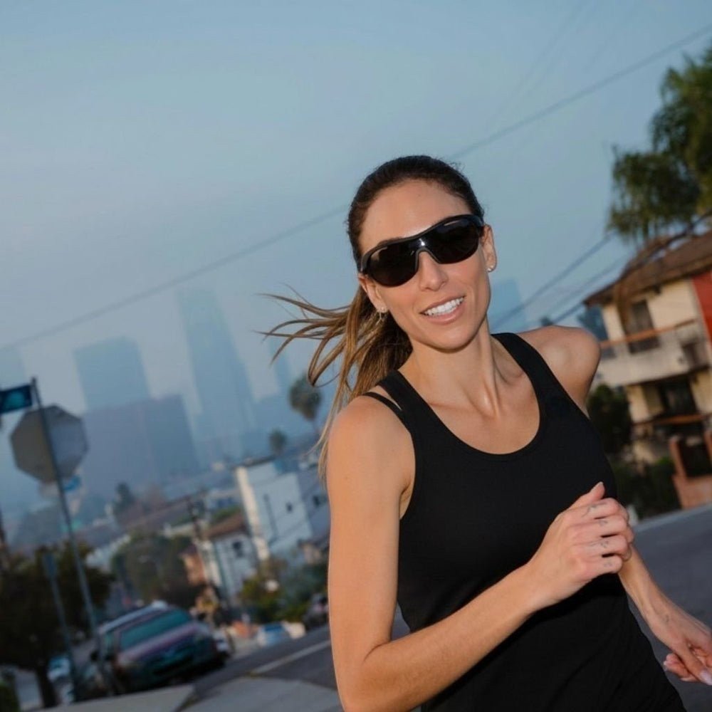 Mulher correndo ao ar livre usando óculos de sol esportivos Goodr Brasil pretos com lentes polarizadas.