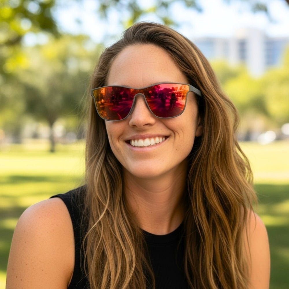 Mulher sorridente usando óculos de sol Goodr Brasil Voight-Kampff Vision com armação cinza e lentes laranja espelhadas