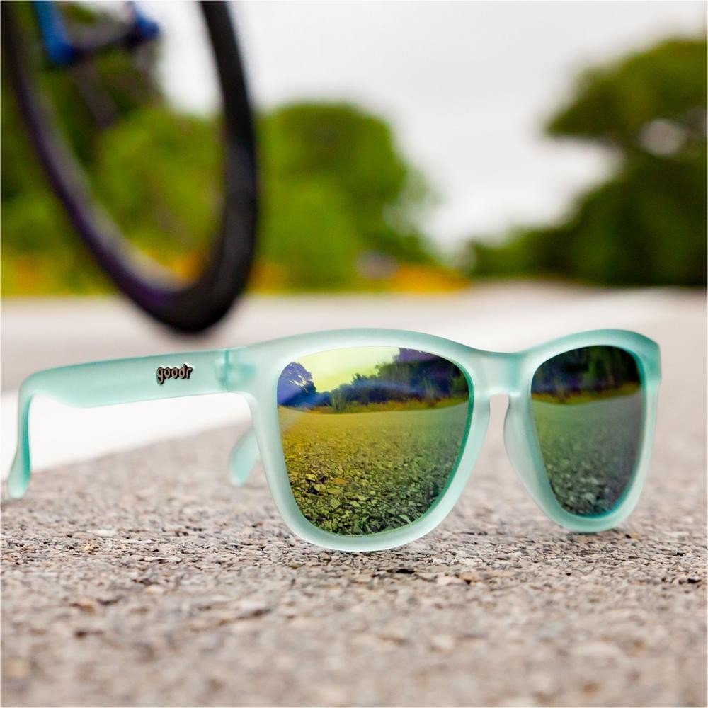 Óculos de sol Goodr Brasil modelo OG com armação verde menta fosca e lentes espelhadas refletindo a estrada.