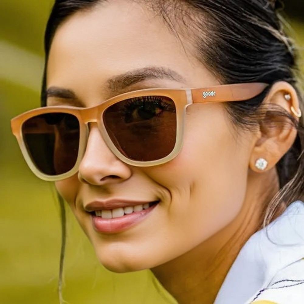 Mulher sorrindo usando óculos de sol Goodr Brasil Three Parts Tee com armação degradê marrom e lentes polarizadas.
