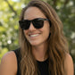 Mulher sorridente usando óculos de sol esportivos pretos Goodr Brasil modelo VRG com lentes polarizadas ao ar livre