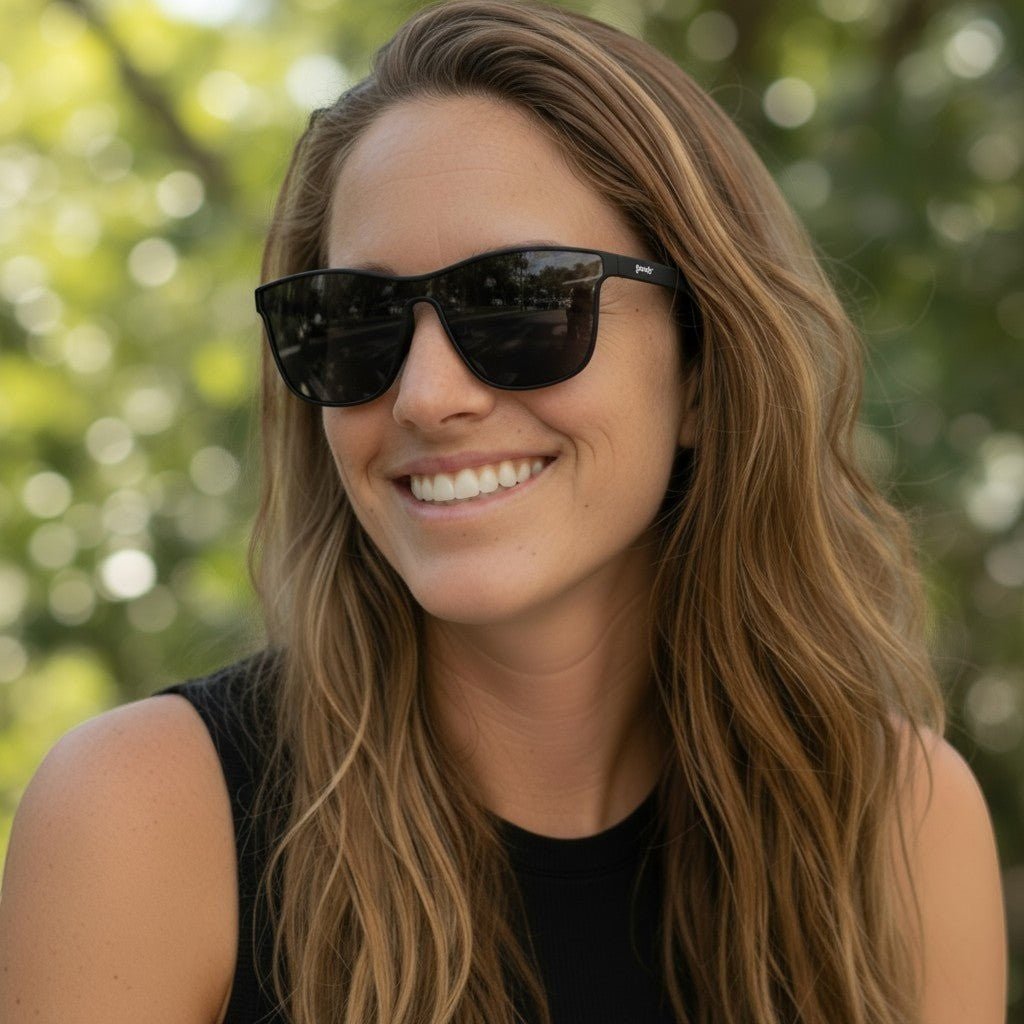 Mulher sorridente usando óculos de sol esportivos pretos Goodr Brasil modelo VRG com lentes polarizadas ao ar livre