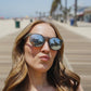Mulher usando óculos de sol Goodr Brasil They Were Out redondo com armação cinza e lentes espelhadas na praia