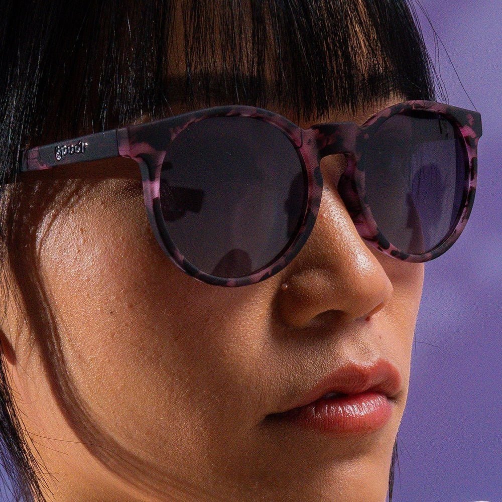 Modelo usando óculos de sol Goodr Brasil Circle G com armação rosa estampada e lentes pretas polarizadas.