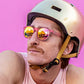 Homem usando óculos de sol Goodr Brasil rosa redondo com lentes espelhadas e capacete, fundo rosa vibrante.