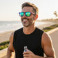 Homem correndo na praia usando óculos de sol Goodr Brasil com armação roxa e lentes polarizadas verdes espelhadas.
