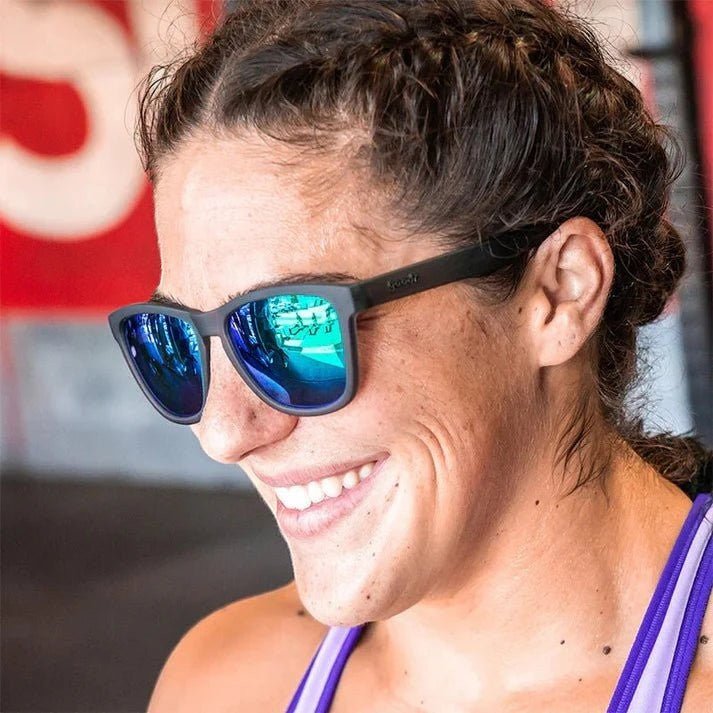 Mulher sorrindo usando óculos de sol Goodr Brasil Silverback Squat Mobility com armação cinza e lentes verdes