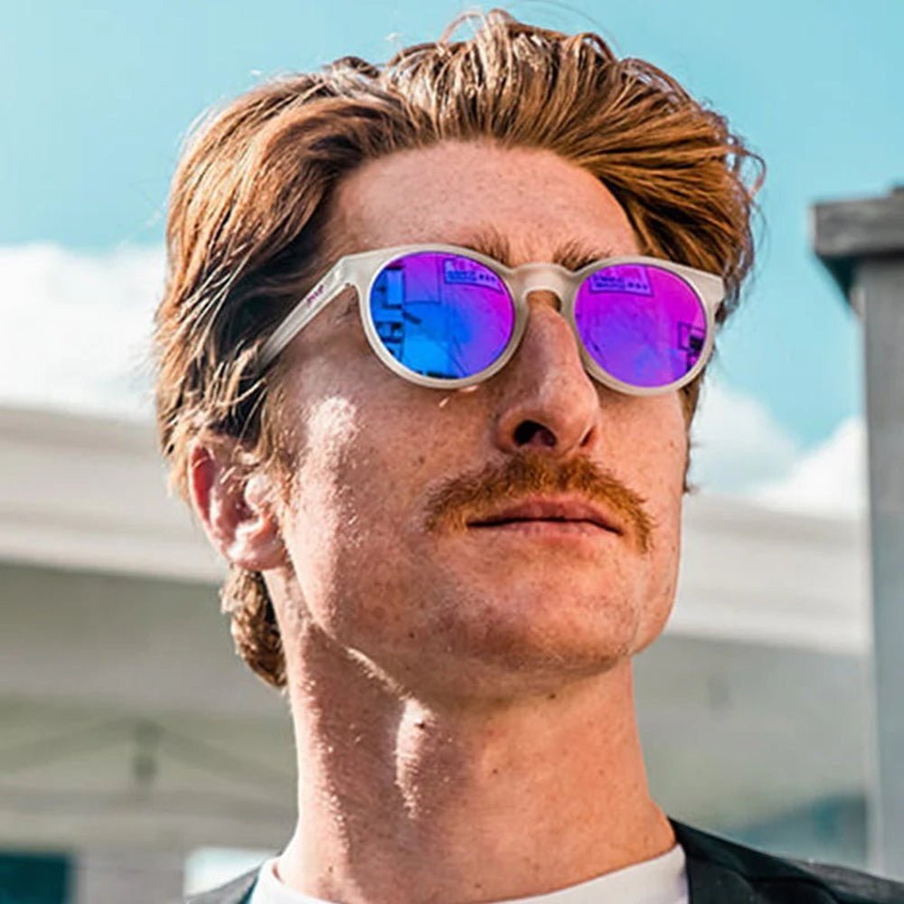 Homem usando óculos de sol Goodr Brasil Circle G com armação transparente e lentes redondas roxas espelhadas ao ar livre