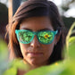 Mulher usando óculos de sol Goodr Brasil verde com lentes espelhadas polarizadas em ambiente externo com girassóis.