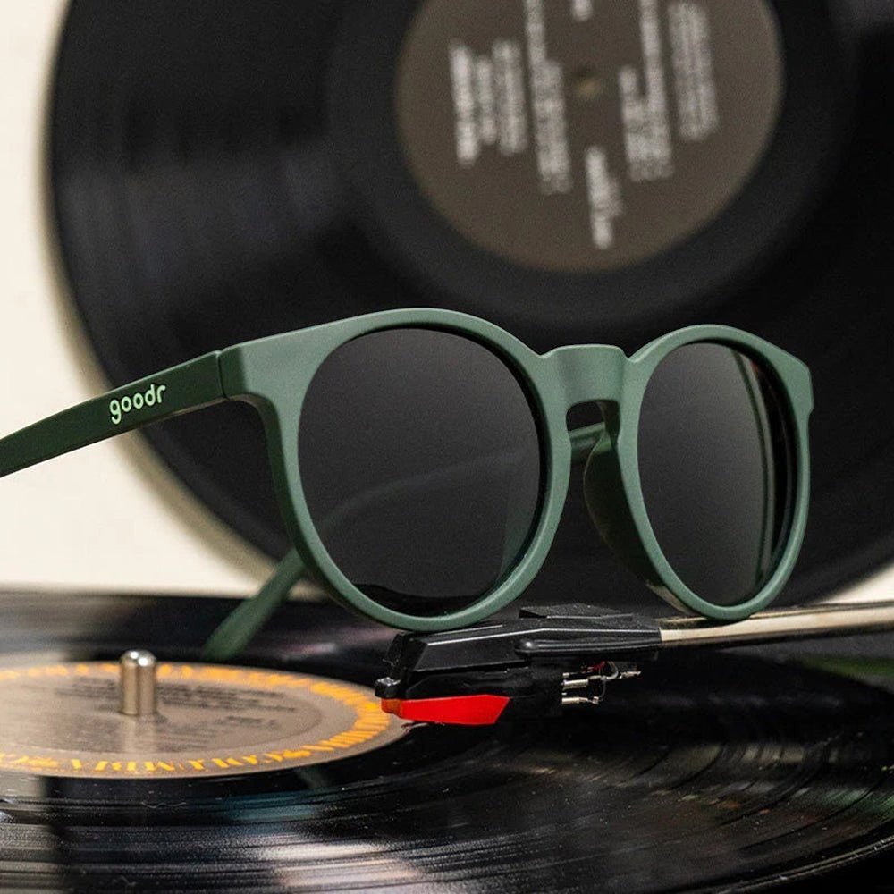 Óculos de sol Goodr Brasil modelo Circle G verde com lentes polarizadas sobre um toca-discos com disco de vinil.