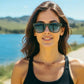 Mulher usando óculos de sol Goodr Brasil BFG verde com lentes espelhadas em ambiente externo ensolarado.