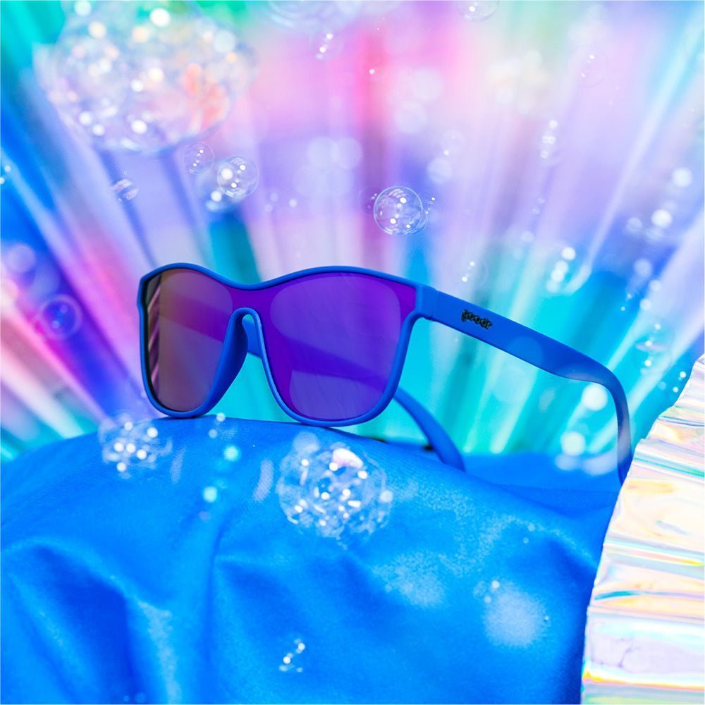 Óculos de sol unissex azul de armação lente única roxa em foco lateral em meio a bolhas de sabão.