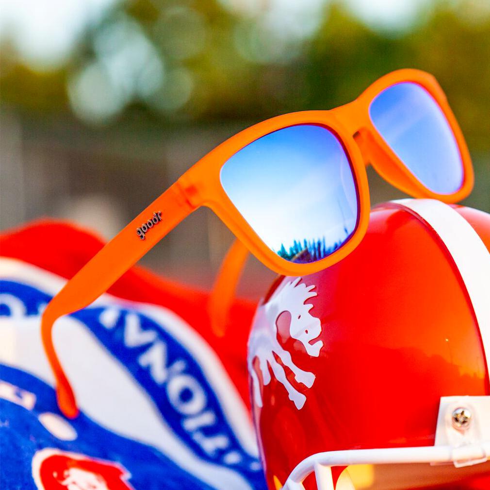 Óculos de sol laranja unissex com armação quadrada e lente azul espelhada, polarizada com proteção UV400. O acessório é leve, confortável e não escorrega ou pula no rosto ao realizar esportes.