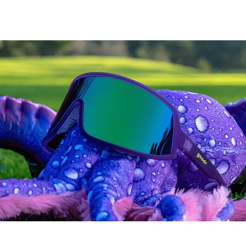 Óculos de sol roxo unissex com armação máscara e lente única verde espelhada, polarizada com proteção UV400. O acessório é leve, confortável e não escorrega ou pula no rosto ao realizar esportes.